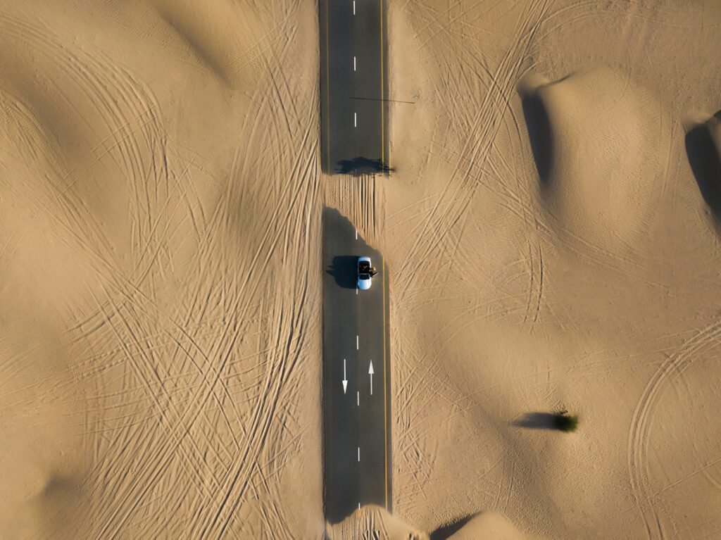 Aerial view of a road cutting through the sand dunes in Dubai's desert landscape.